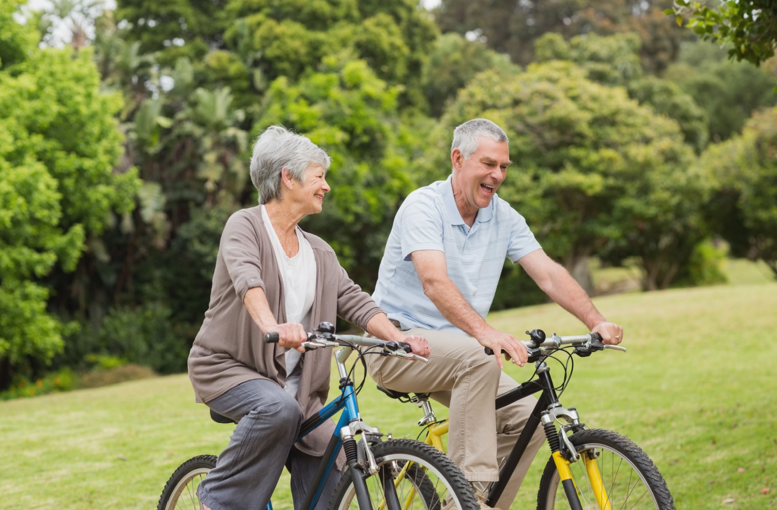 An older adult couple biking by the park.
