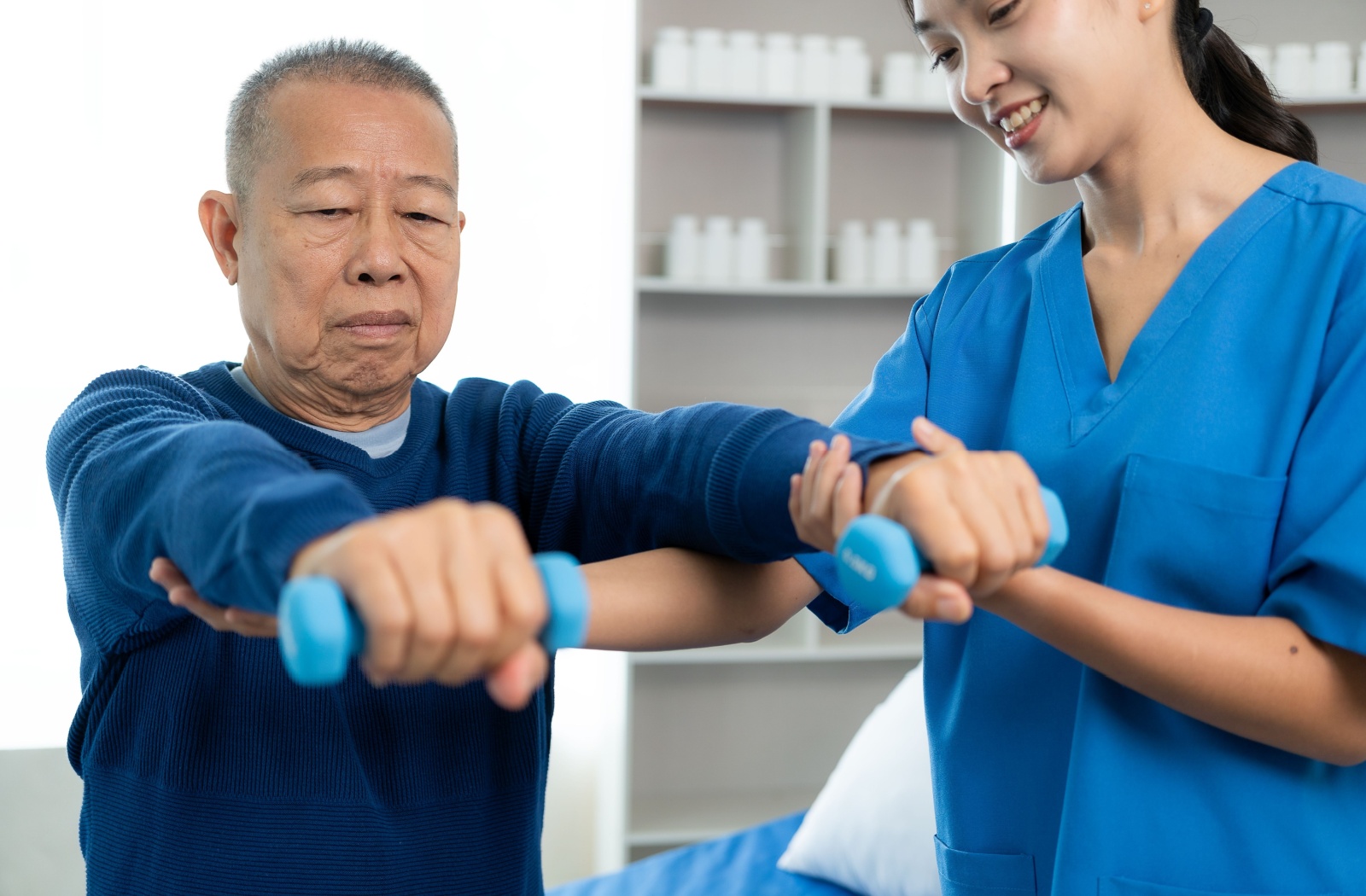 Asian woman physio therapist helping an Asian senior man with an arm exercise.
