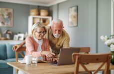 A senior couple in their home smiling while researching independent living communities on their computer.