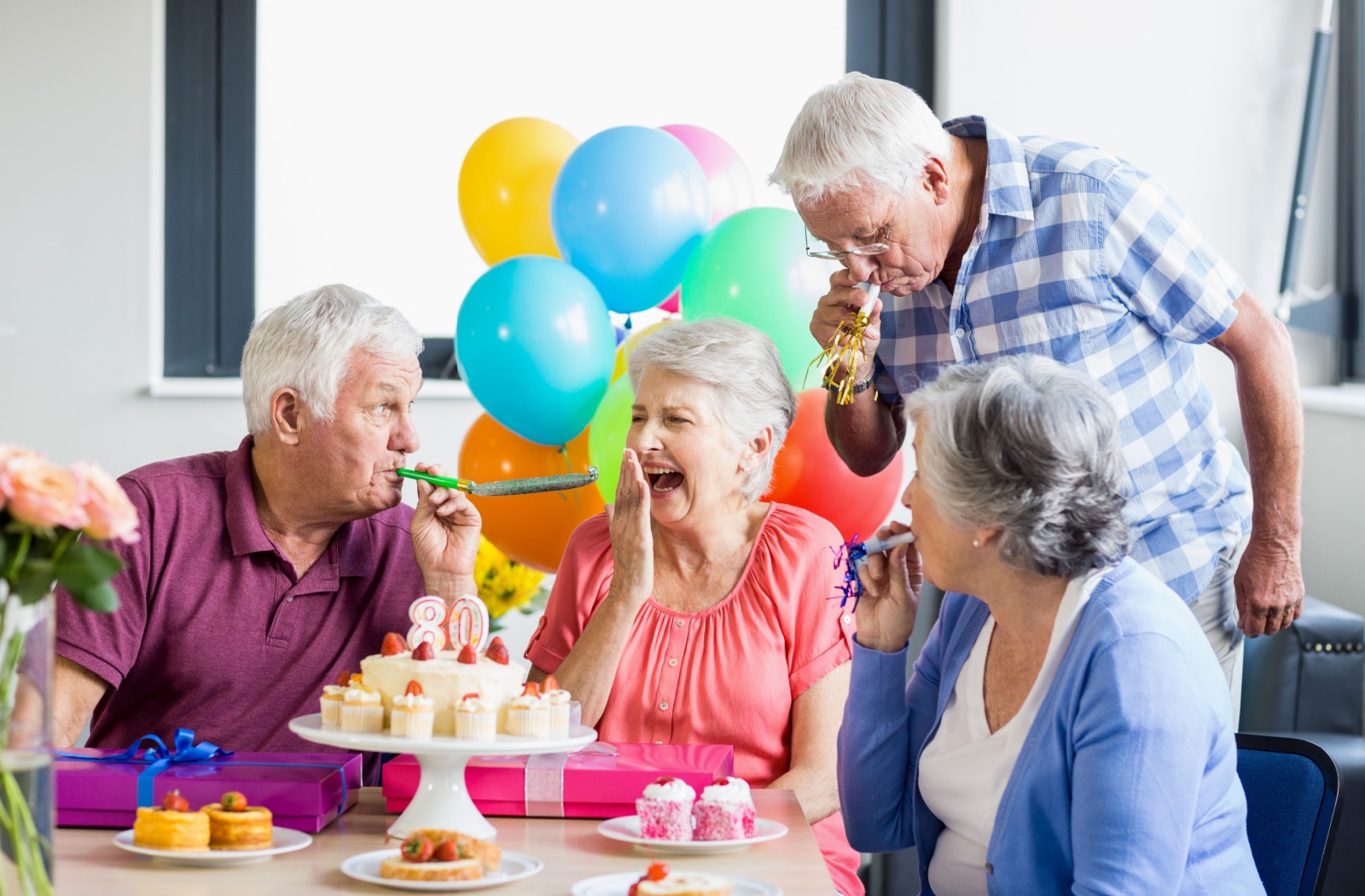 A group of seniors in independent living celebrating a birthday with balloons, cupcakes, and noisemakers.
