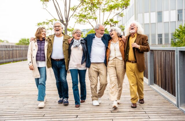 6 senior friends walking across a bridge with their arms around one another during a tour of Albuquerque.