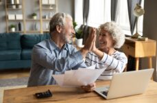 An excited senior couple at home high-fiving in front of their computer after making a financial plan to move to senior living.