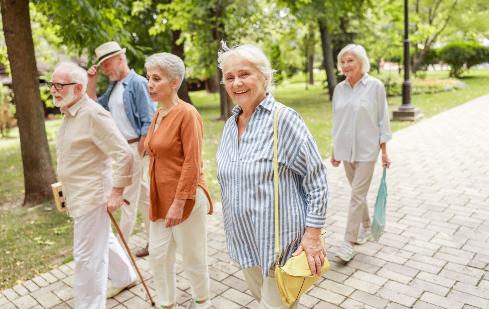 A group of five seniors are chatting as they walk together around their retirement community on a sunny day.