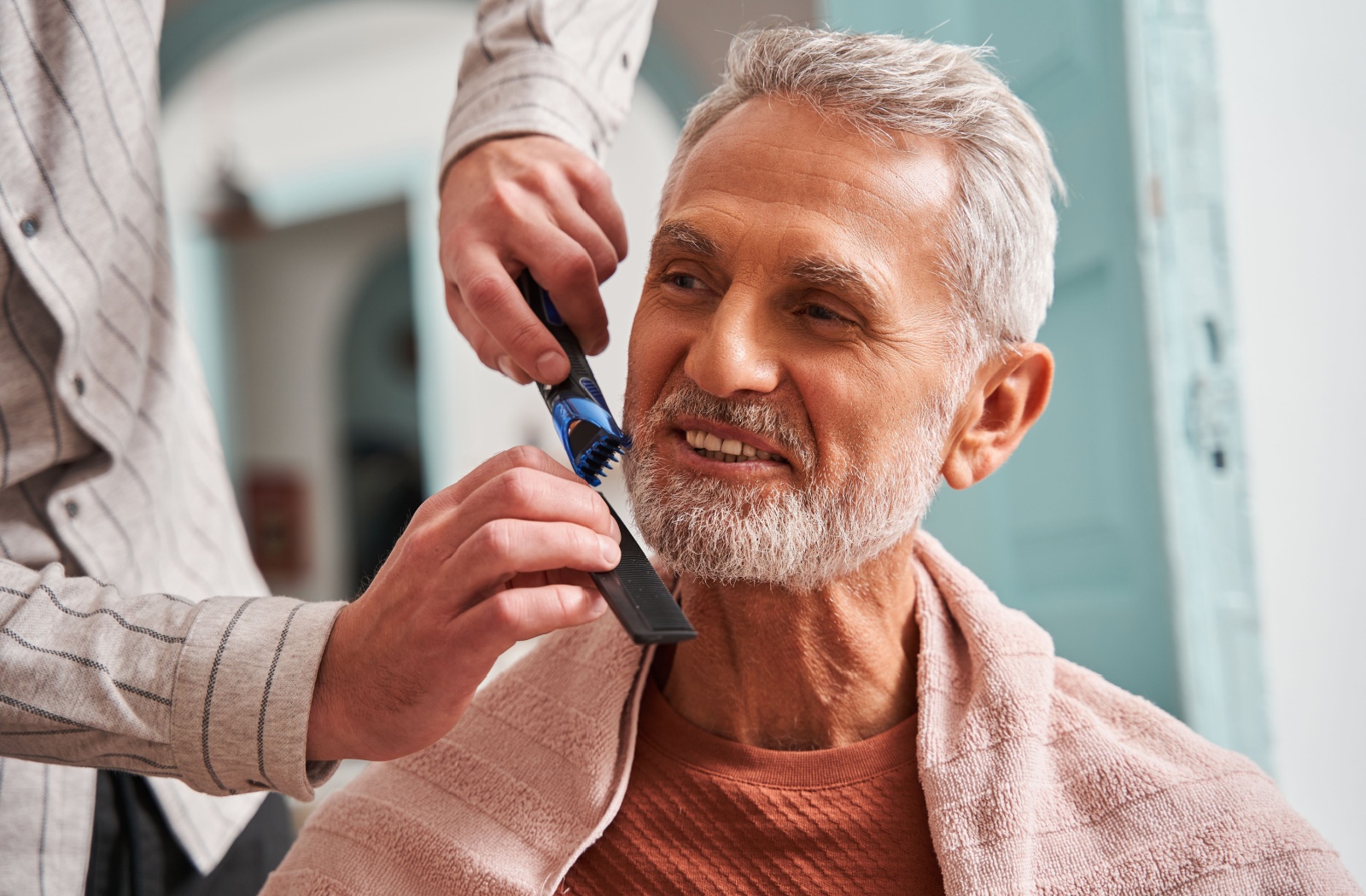 A smiling older adult receiving a beard trim from the community barber.